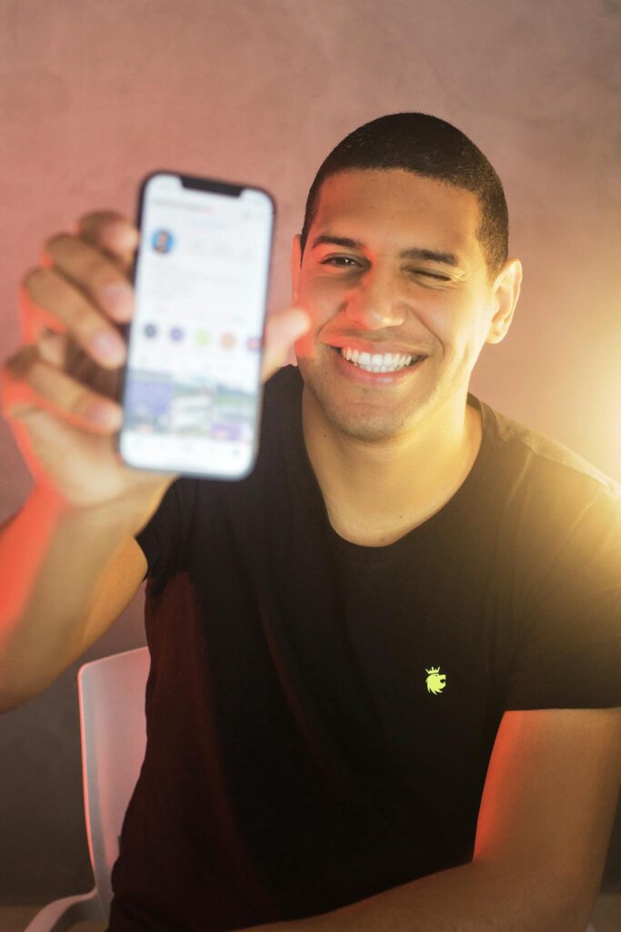 Happy man in a black shirt using a smartphone indoors, smiling and winking.