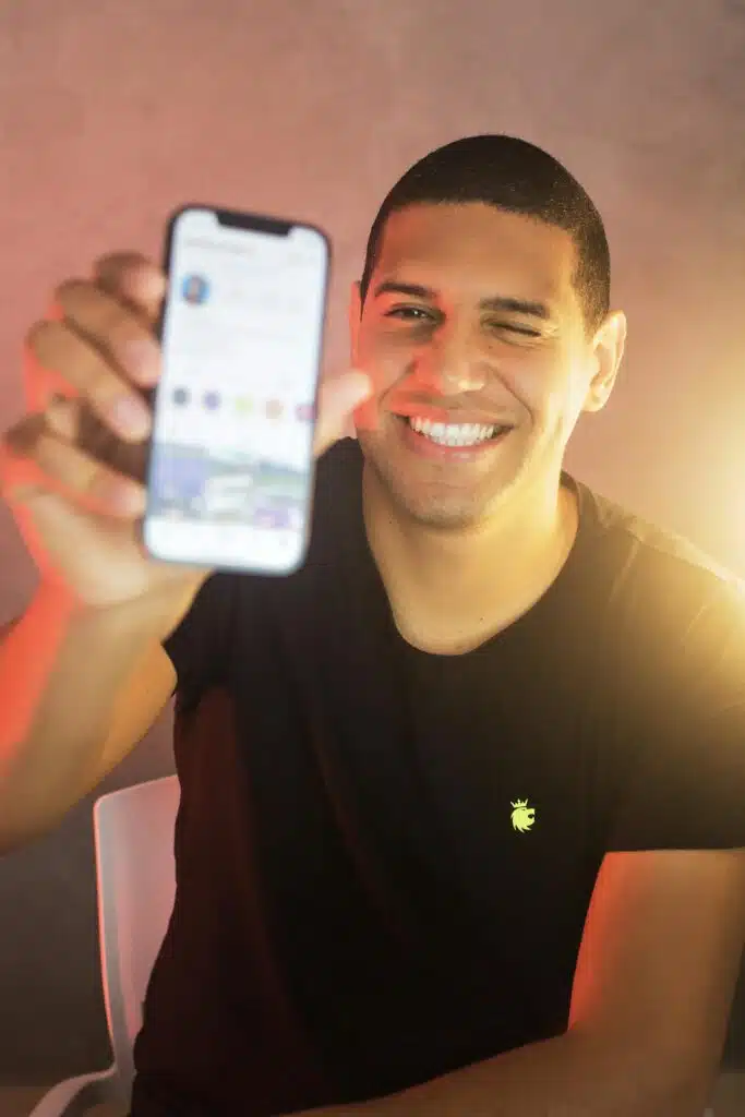 Happy man in a black shirt using a smartphone indoors, smiling and winking.